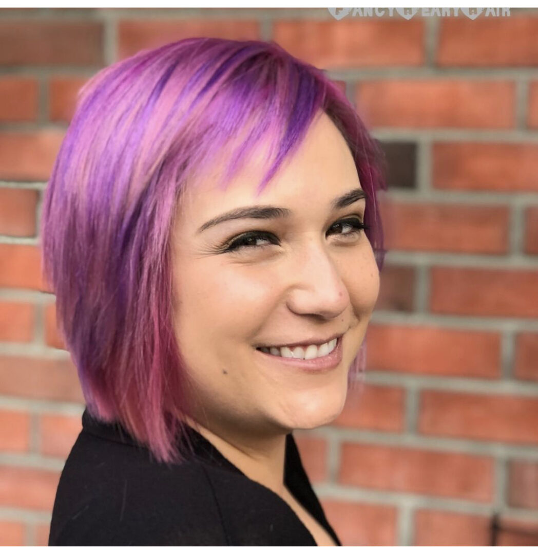 A woman with purple hair smiling for the camera.