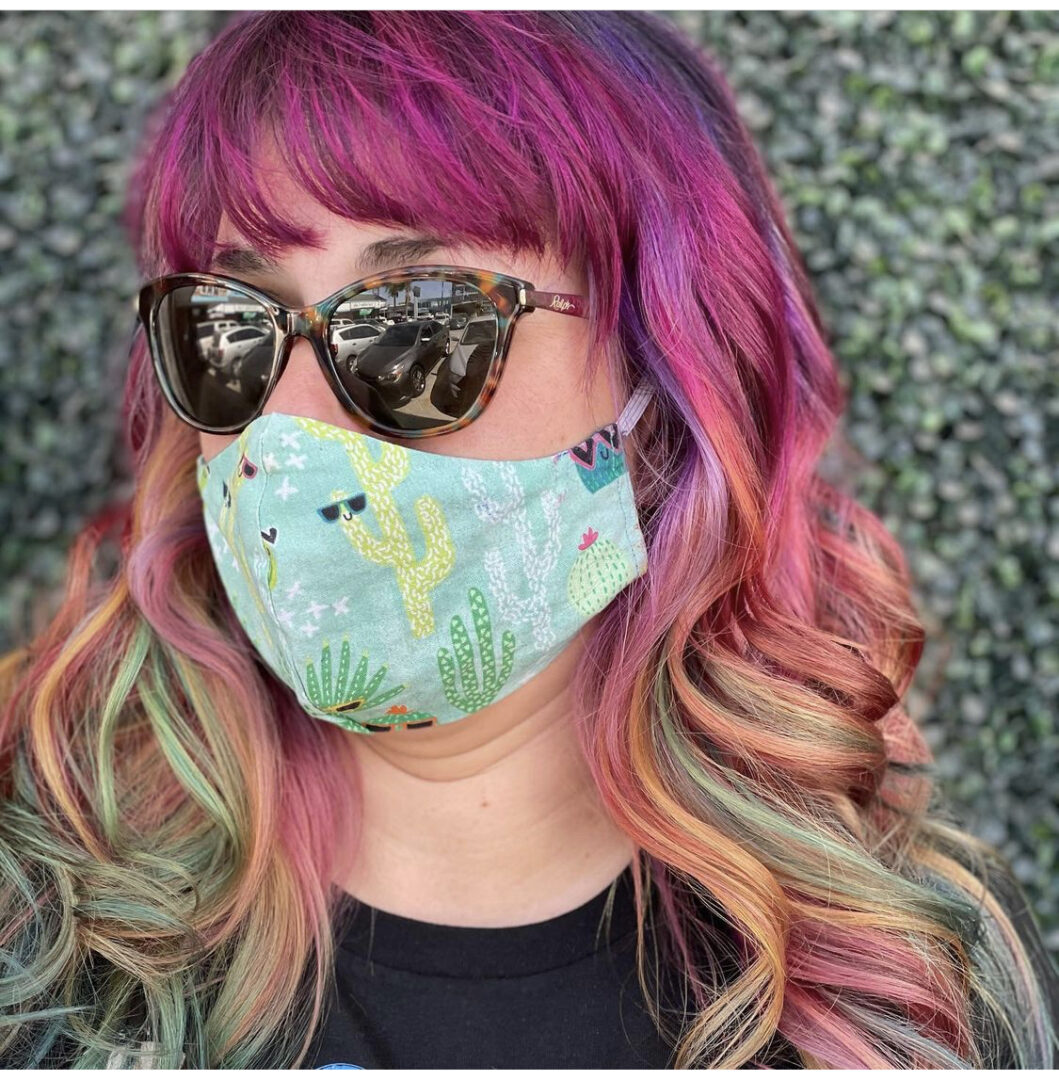 A woman with pink hair wearing sunglasses and a mask.