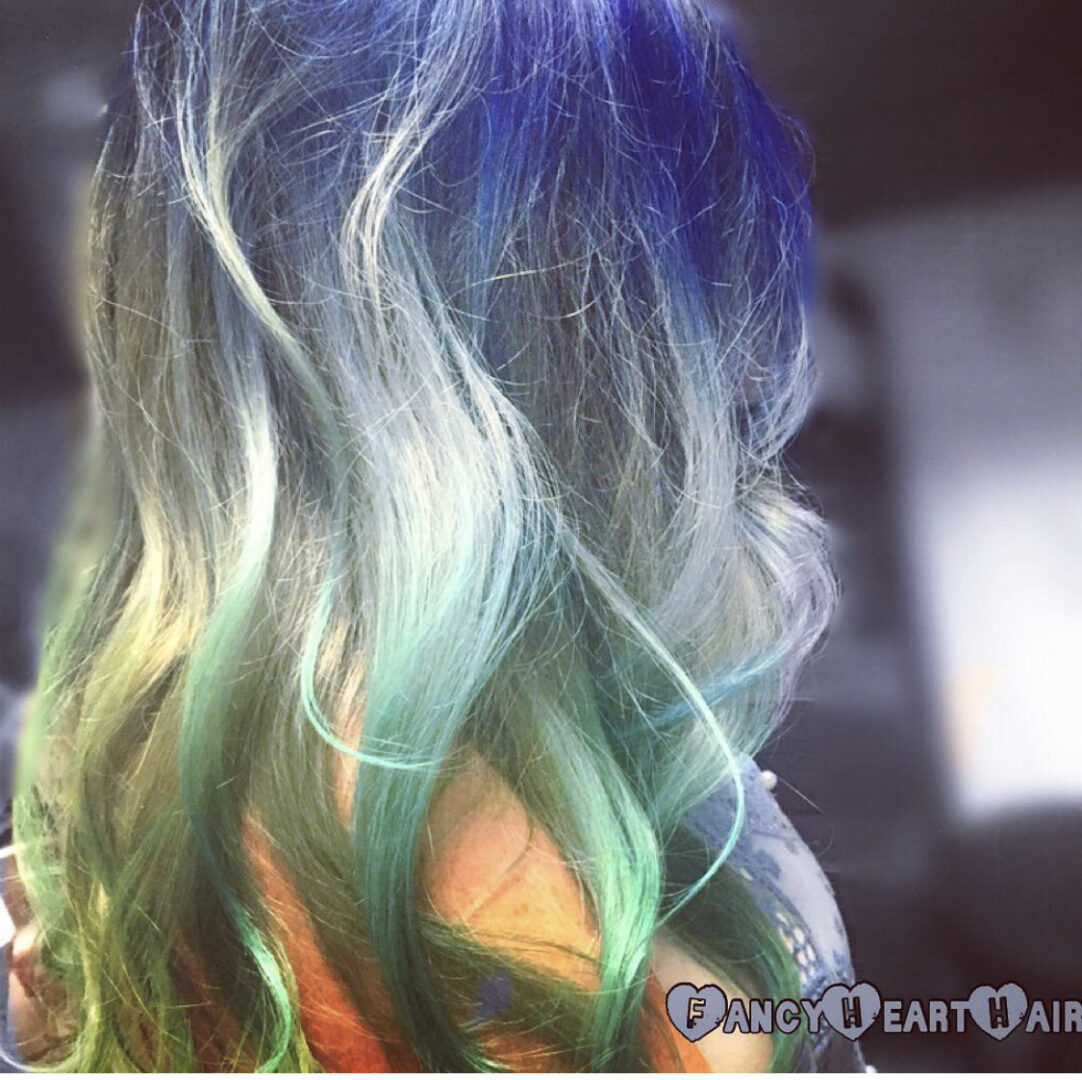 A woman with blue and green hair is looking at the camera.